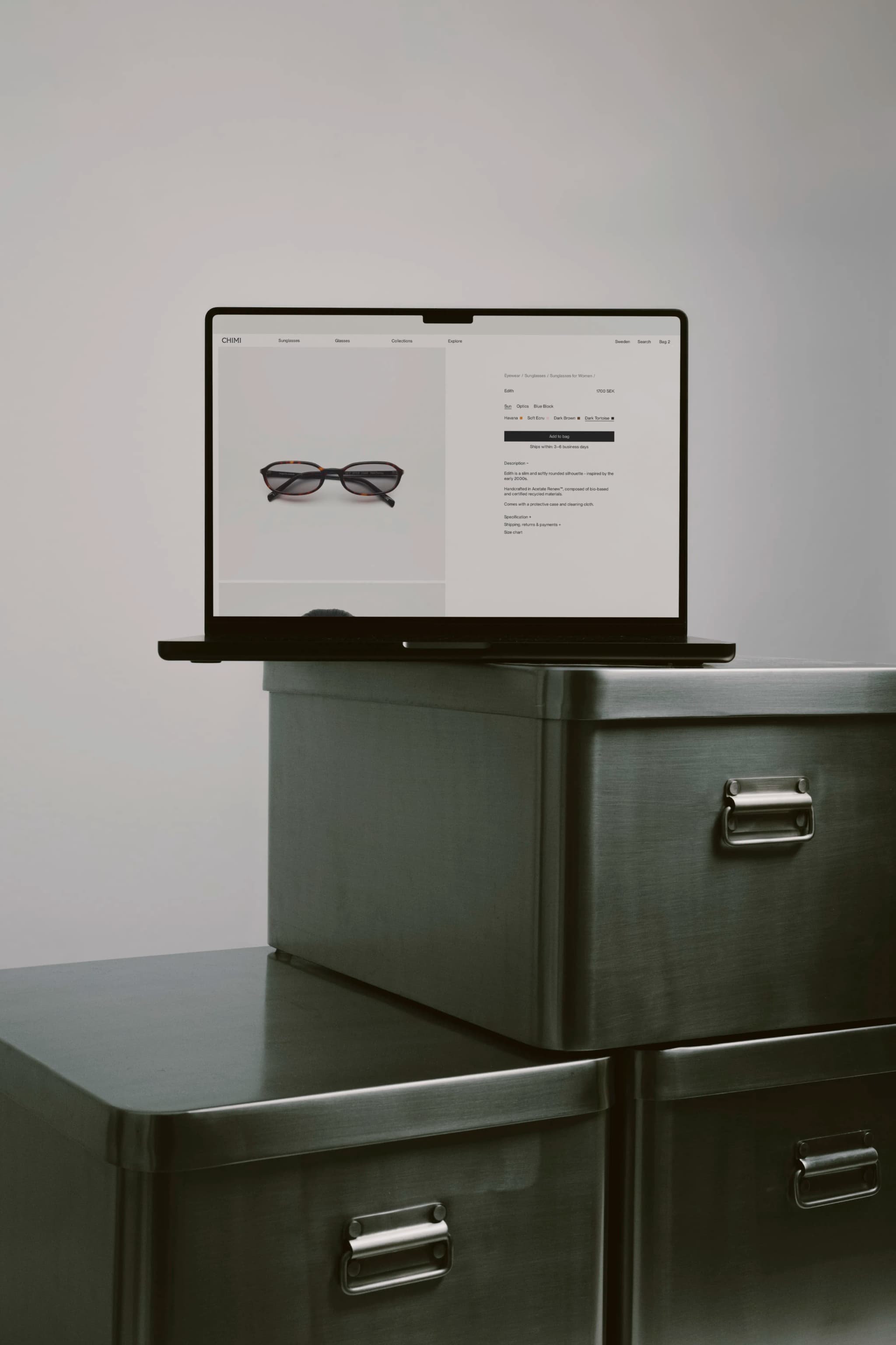 Laptop displaying the Chimi store sits on stacked metal boxes against a plain background.